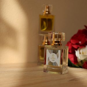 A close-up of luxurious perfume bottles beside red and white roses, elegantly lit by soft sunlight.