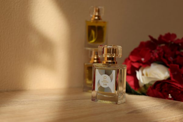 pexels photo 26600130 26600130 A close-up of luxurious perfume bottles beside red and white roses, elegantly lit by soft sunlight.