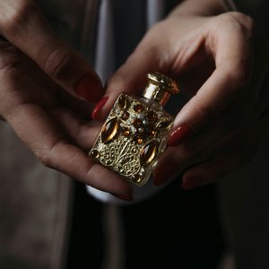 Crop faceless female with red manicure demonstrating small vintage golden perfume bottle decorated with natural stones and carved details