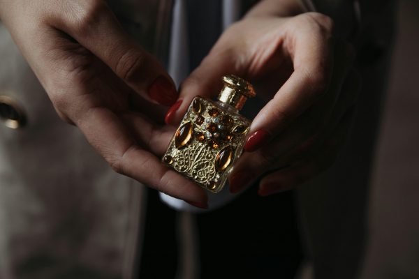 pexels photo 3615228 3615228 Crop faceless female with red manicure demonstrating small vintage golden perfume bottle decorated with natural stones and carved details